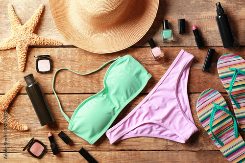 Colorful bikini, cosmetics and beach accessories on wooden background