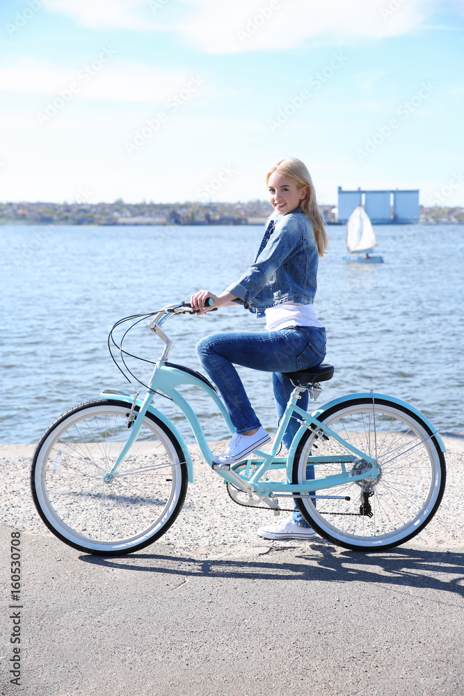 Fototapeta premium Young smiling girl with bicycle on embankment