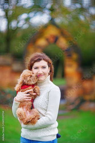 Woman hugging her little pet standing on the background of an old wall in an English garden