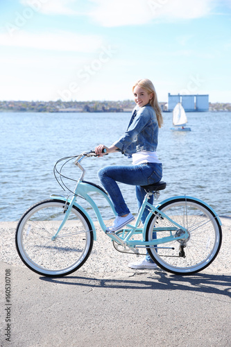 Young smiling girl with bicycle on embankment