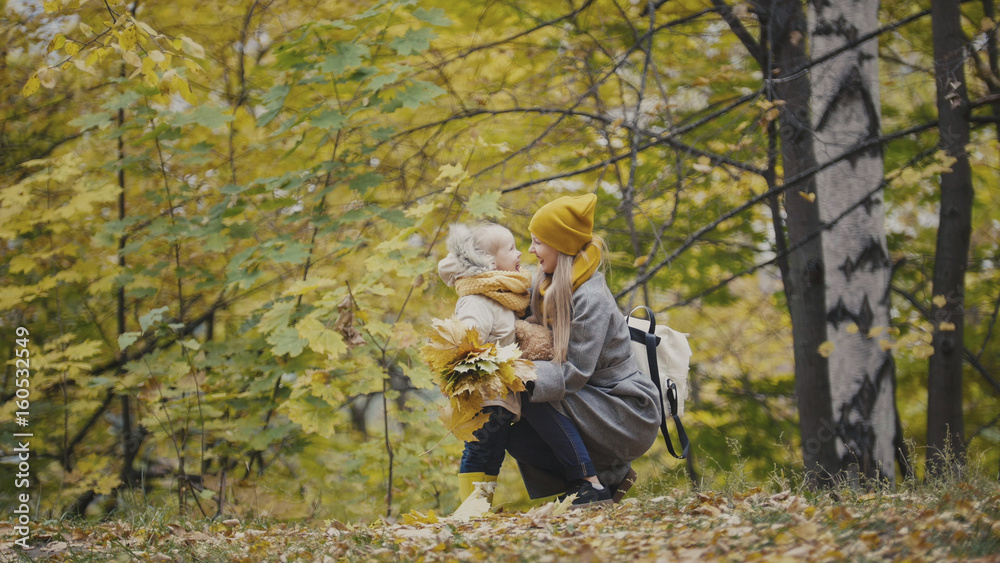 Mother and daughter together among yellow leaves in autumn park