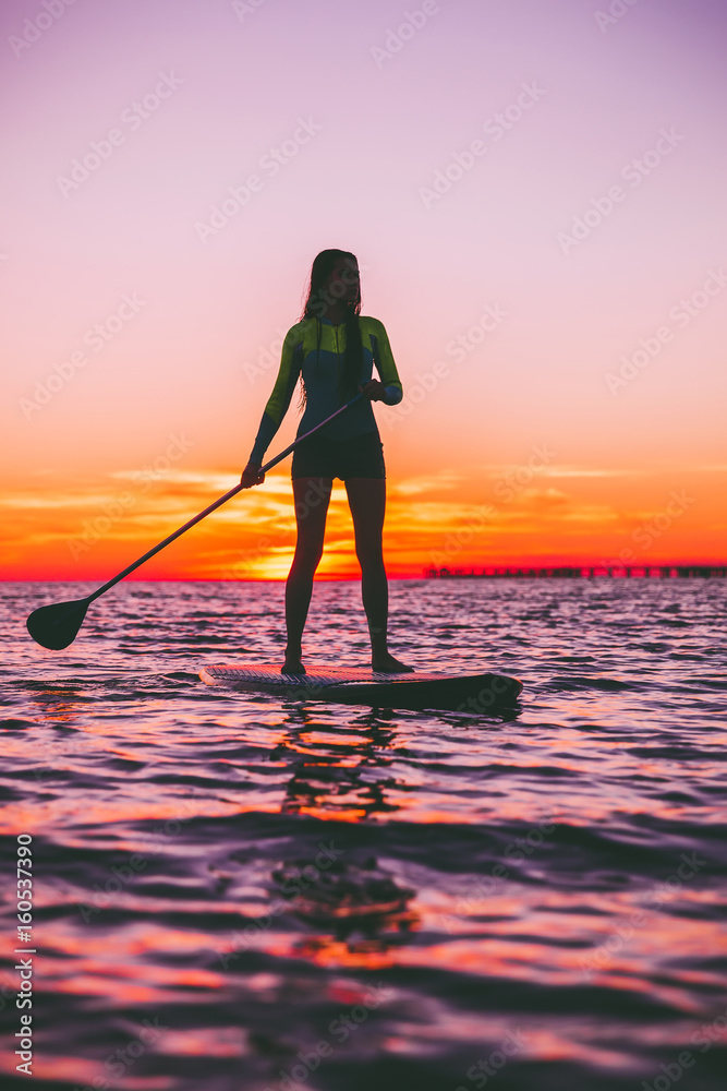 Girl stand up paddle boarding on a quiet sea with warm sunset colors