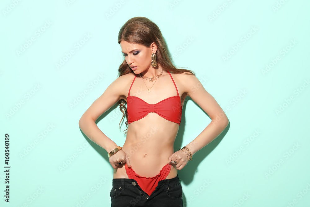 Beautiful young woman in bikini and trousers on color background Beautiful young woman in bikini and trousers on color background
