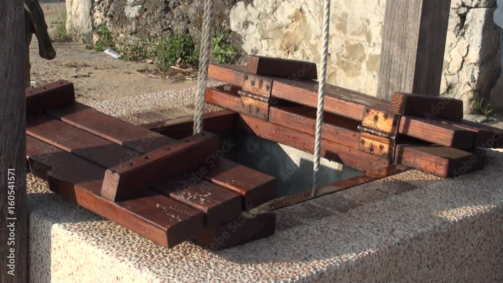 A person inserts two buckets into a water well to draw water with the