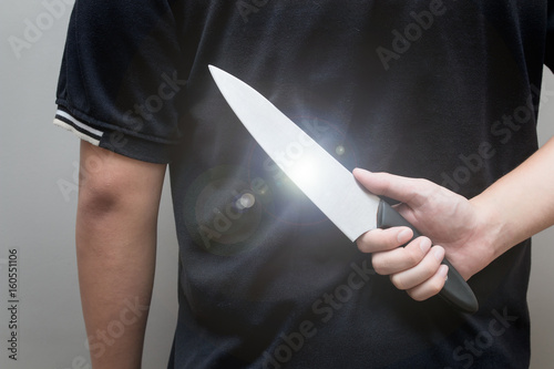 Closeup of a young man hand  holding knife behind his back and waiting for a woman to attack  concept of danger  stress  unfulfillment  risk.