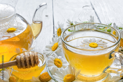 cup of herbal tea with chamomile flowers and honey and teapot photo