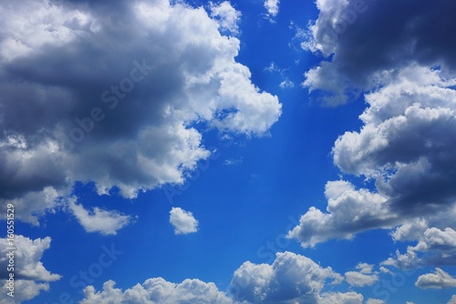 Голубое яркое небо с серо белыми облаками и солнечными лучами