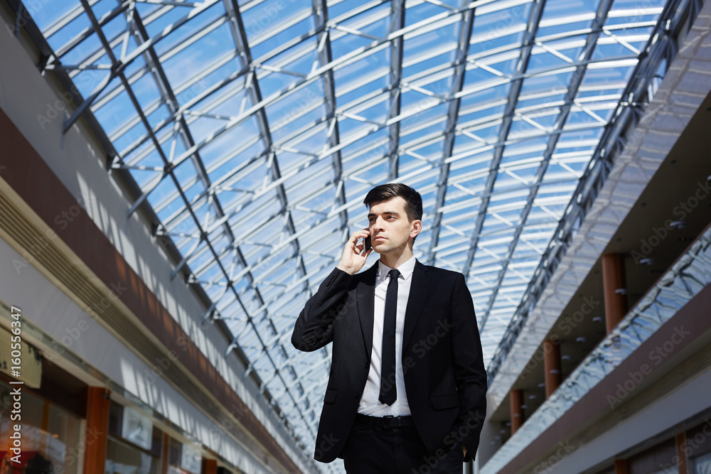 Portrait of successful confident businessman speaking by phone looking away under glass ceiling in modern office building Portrait of successful confident businessman speaking by phone looking away under glass ceiling in modern office building