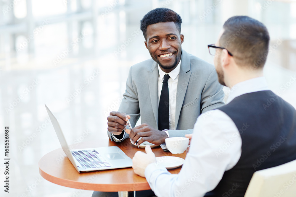 Portrait of successful African-American businessman smiling while discussing deal with partner during meeting at coffee break - obrazy, fototapety, plakaty 