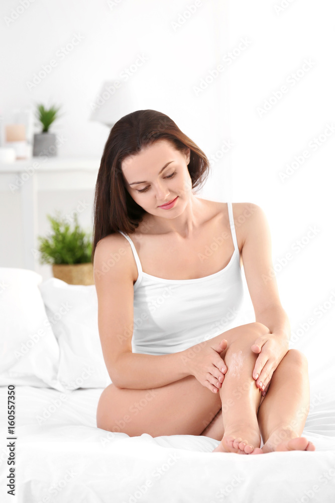 Beautiful young woman in bedroom applying cream onto legs Beautiful young woman in bedroom applying cream onto legs