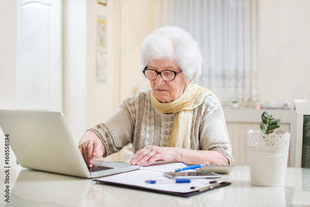 Senior woman going over financial bills with laptop at home. Senior woman going over financial bills with laptop at home.
