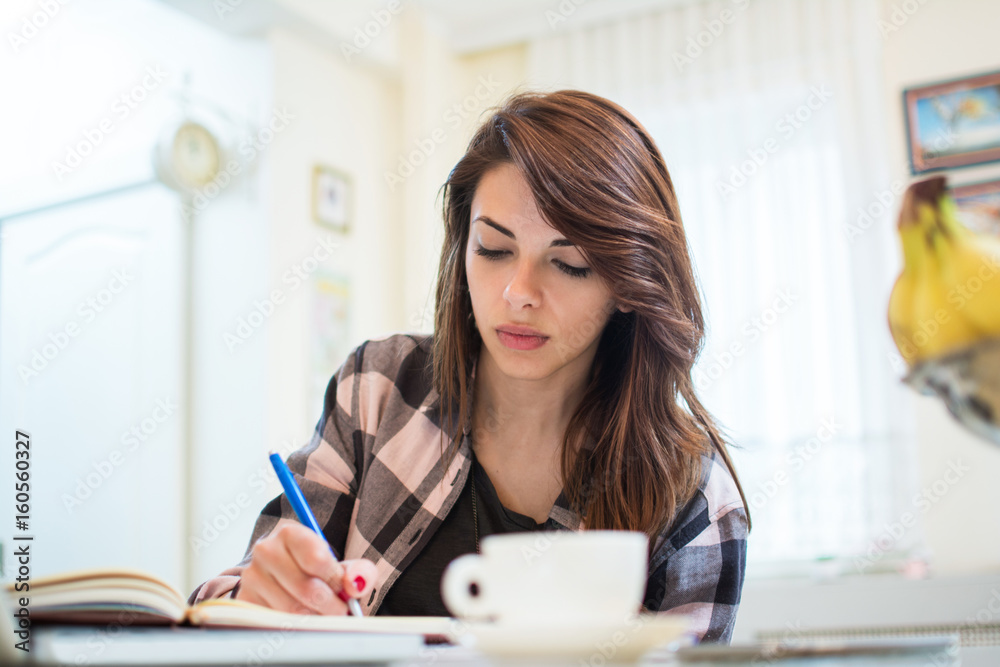 Portrait of serious female student doing homework while having morning coffee at home. Portrait of serious female student doing homework while having morning coffee at home.