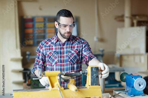 Young man using woodworking machine in workshop