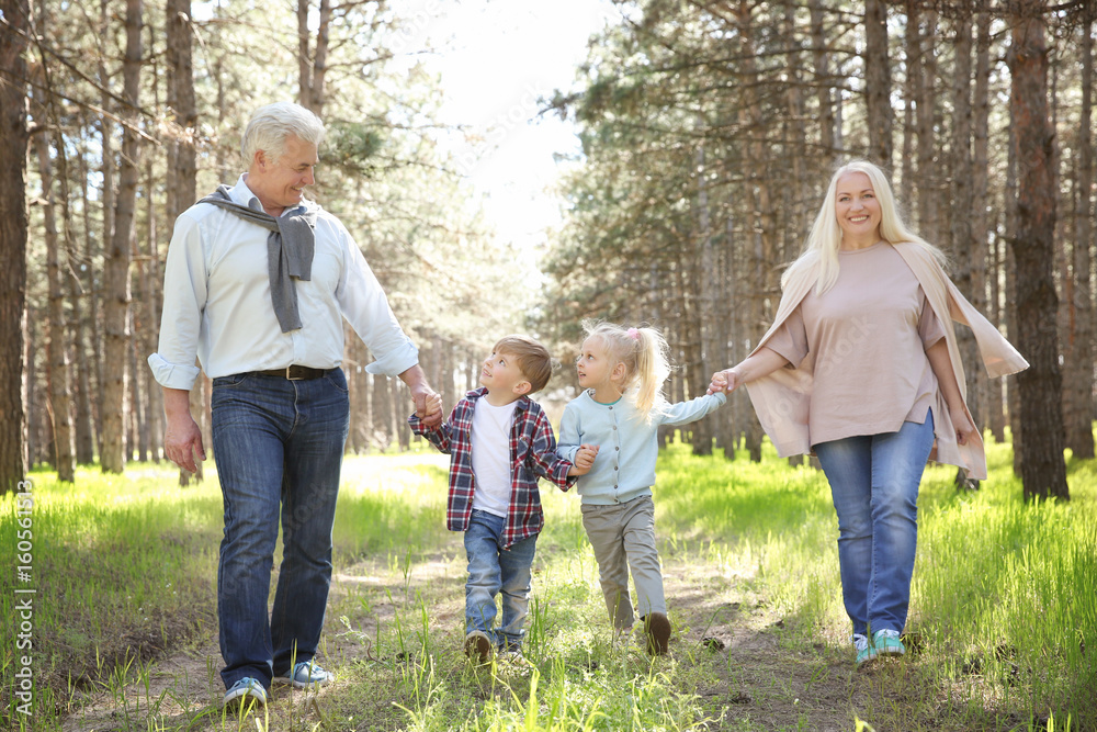 Happy grandparents with little children in forest on sunny day