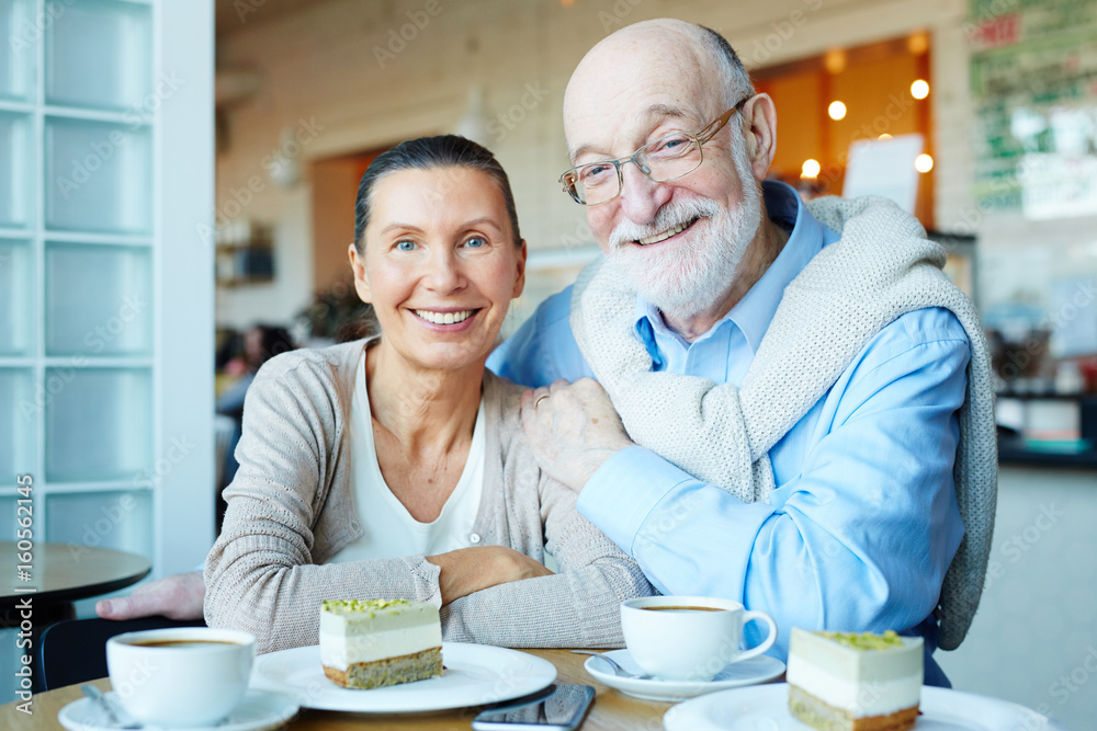 Affectionate seniors lookking at camera while sitting in cafeteria