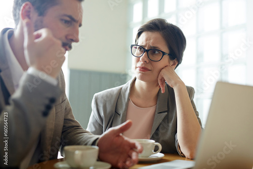 Portrait of two confused business people, man and woman, solving work problem during meeting in cafe