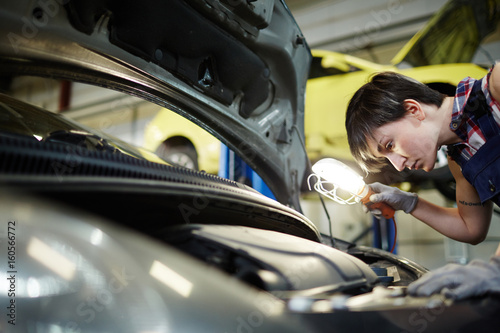 Car repair specialist with lamp inspecting engine