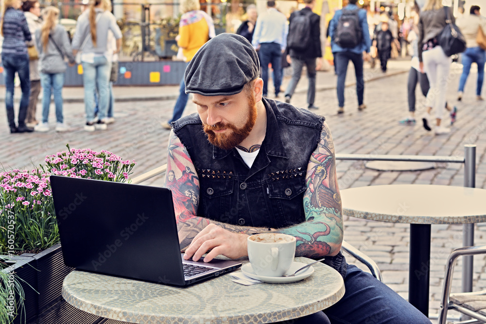 Bearded male using laptop in a summer street cafe.
