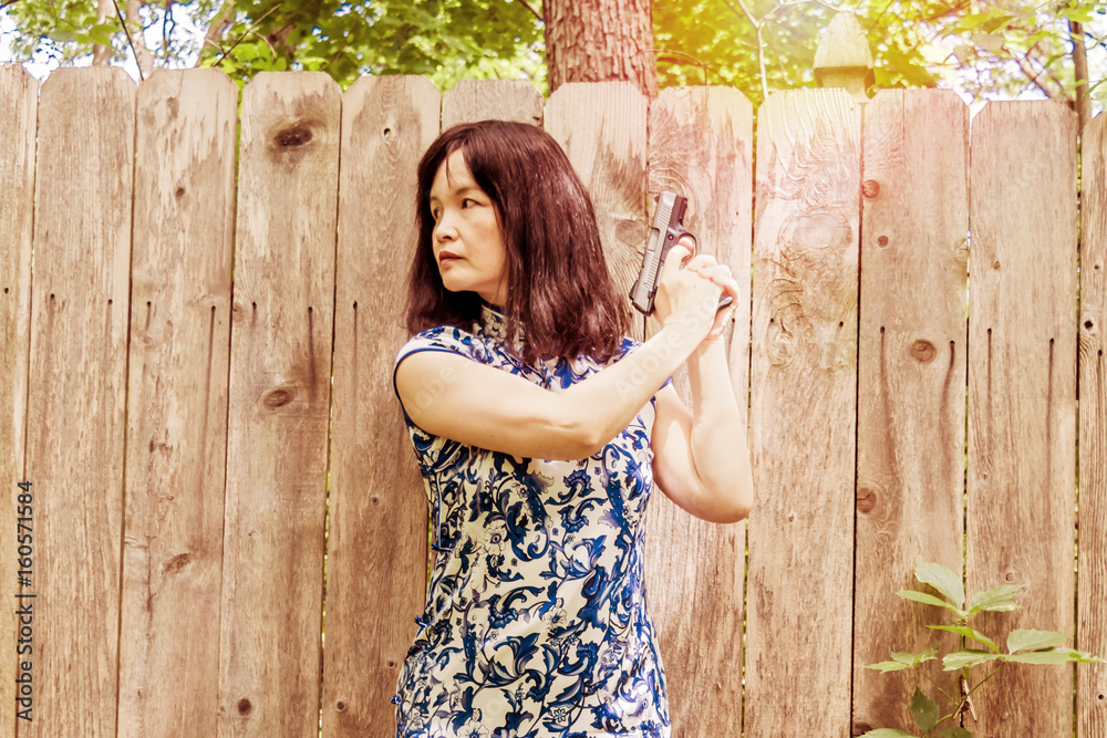 Obraz premium An Asian woman is holding a pistol in front of a wood fence