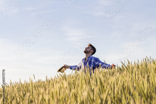 Принти на полотні Young guy with hans up and with hat on his hand in the middle of the field