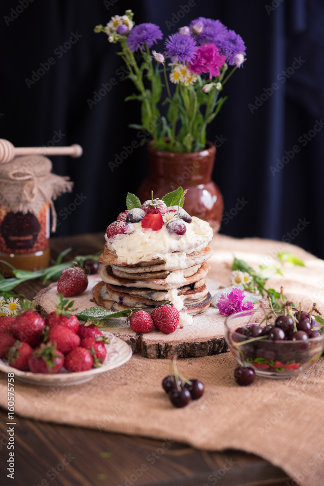 Delicious pancakes with berries and cream on the authentic wooden stand. Summer food still life concept.