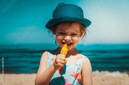 Little and cute girl eating ice cream on the beach on vacation