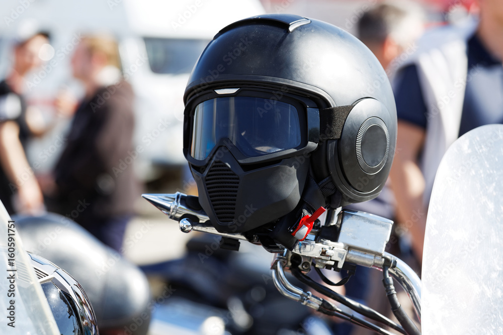 Black moto helmet on motorcycle handlebars against blurred background Black moto helmet on motorcycle handlebars against blurred background