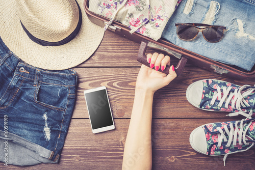 Travel preparations with casual summer clothes on wooden table. Top view