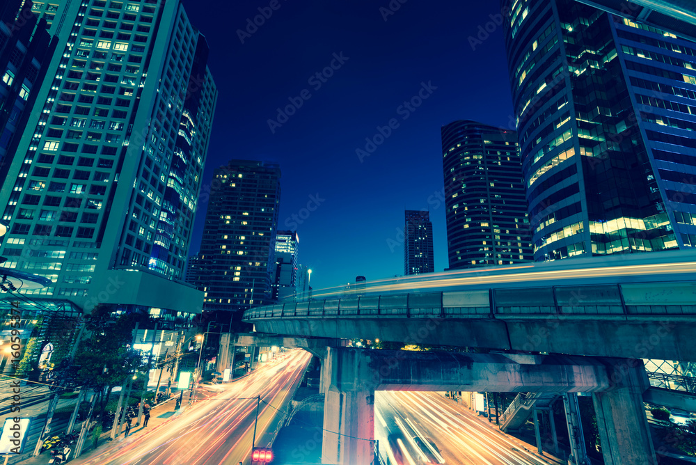 Fototapeta premium Photo of commercial office buildings exterior. Night view at bottom skyscrapers with light of traffic rush, long exposur in Bangkok