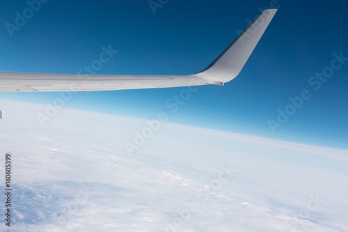A view of the wing of the plane against a background of white clouds and blue sky.