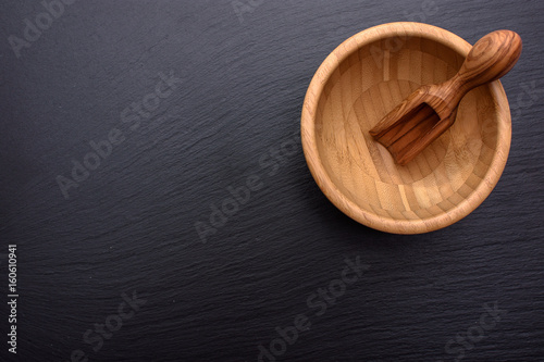 A scoop of olive tree lies in a wooden cup on the background of a black shale stone