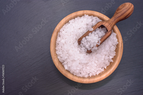 Salt lies in a wooden cup in it lies a wooden scoop in the center of a black stone board