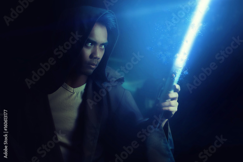 Εκτύπωση καμβά Young warrior holding a lightsaber on a dark background