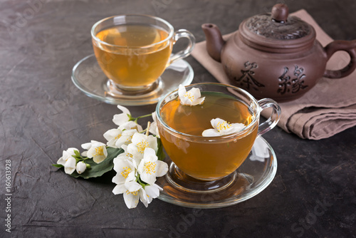 Glass cups of tea and tea pot with jasmine on a dark background.