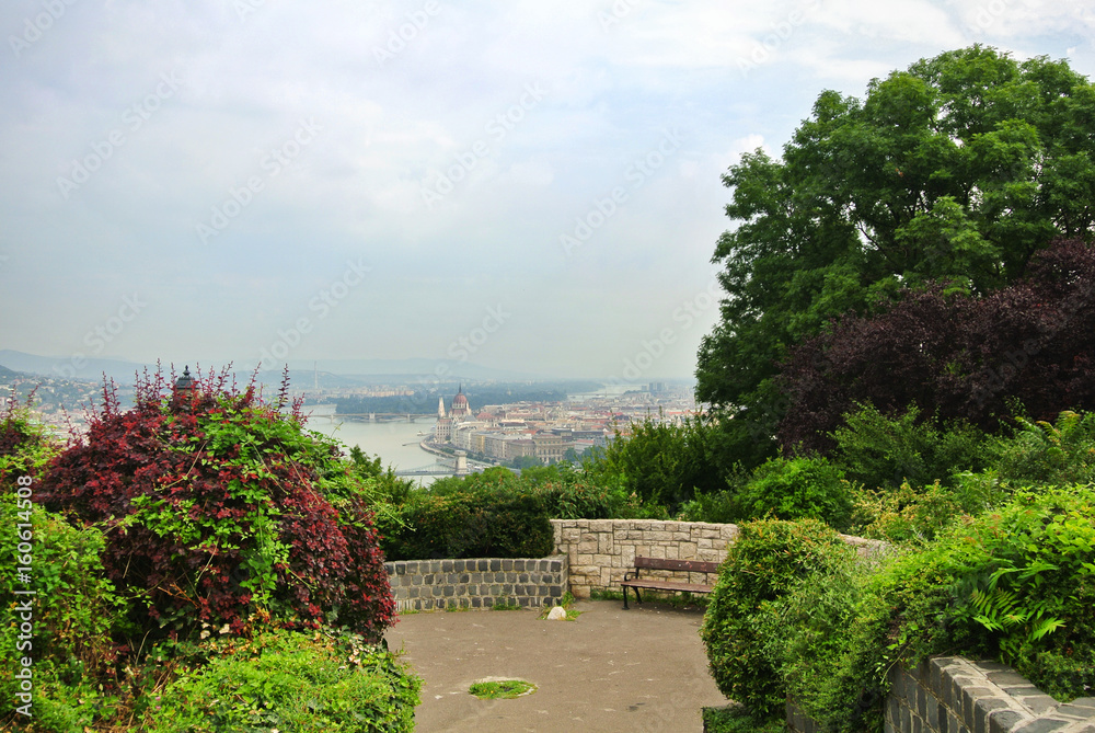A viewpoint at the park over the hill at Budapest, a view to Danube river and a building of Parliament and a bench under a brick wall, Hungary.