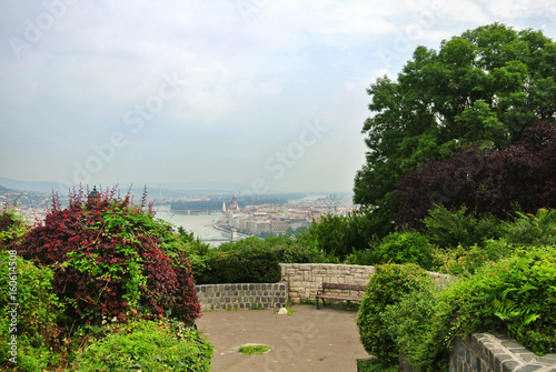 Photography A viewpoint at the park over the hill at Budapest, a view to Danube river and a building of Parliament and a bench under a brick wall, Hungary