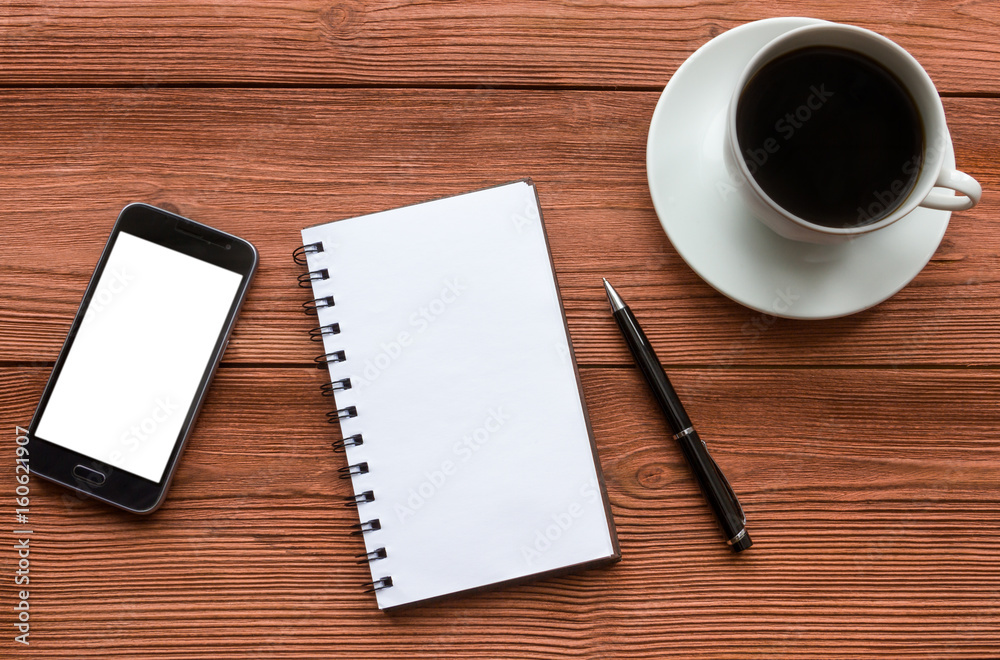 Empty notebook and ball pen with a cup of coffee, phone, screen mock up against the background of the office desk. Business concept with copy space for any design Empty notebook and ball pen with a cup of coffee, phone, screen mock up against the background of the office desk. Business concept with copy space for any design