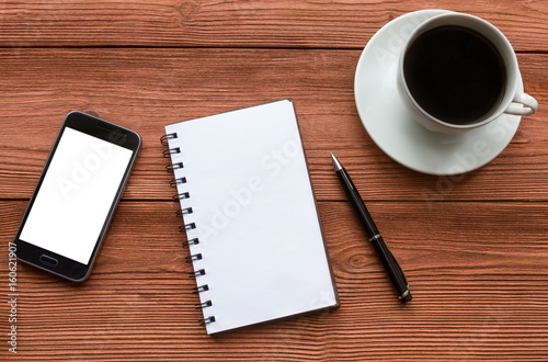 Empty notebook and ball pen with a cup of coffee, phone, screen mock up against the background of the office desk. Business concept with copy space for any design