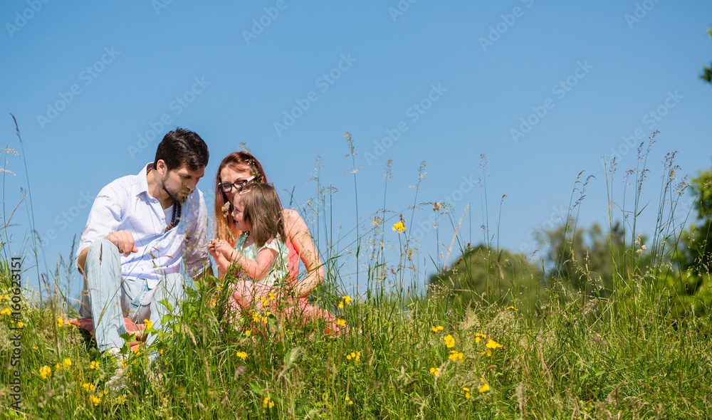 Family cuddling sitting at meadow on a summer day with blue sky Family cuddling sitting at meadow on a summer day with blue sky
