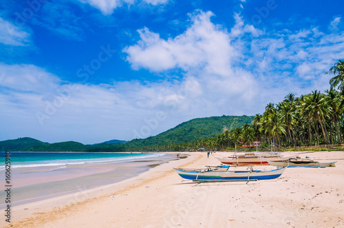 Local boats on wide Nacpan Beach on sunny day. El Nido, Palawan, Philippines