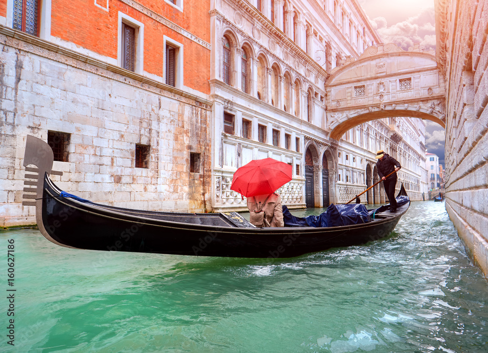 Woman with a red umbrella in Gondola passing over Bridge of Sighs in Venice