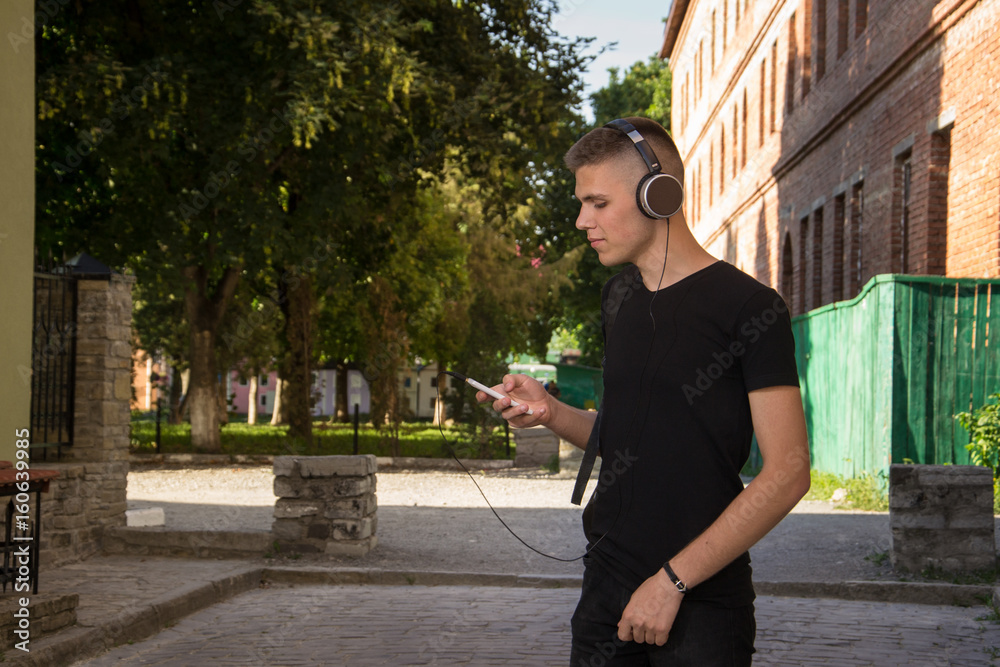 smaling teenager in headphones on the street. Young handsome man standing with phone in hand