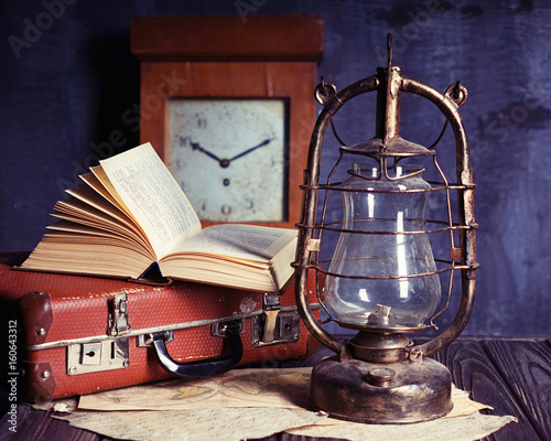 vintage travel still life with kerosene lamp, book and suitcase 