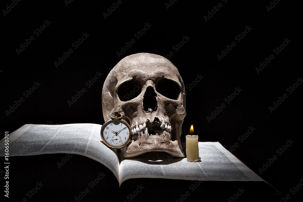 Human skull on old open book with burning candle and vintage clock on black background under beam of light Human skull on old open book with burning candle and vintage clock on black background under beam of light
