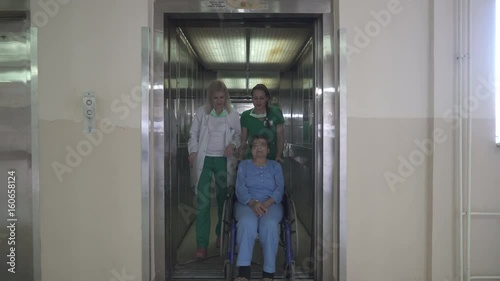 Wallpaper Mural Two Caucasian young nurses are transporting old female patient in wheelchair, they are coming out of elevator and walking through the hospital building hallway, steadicam tracking shot Torontodigital.ca