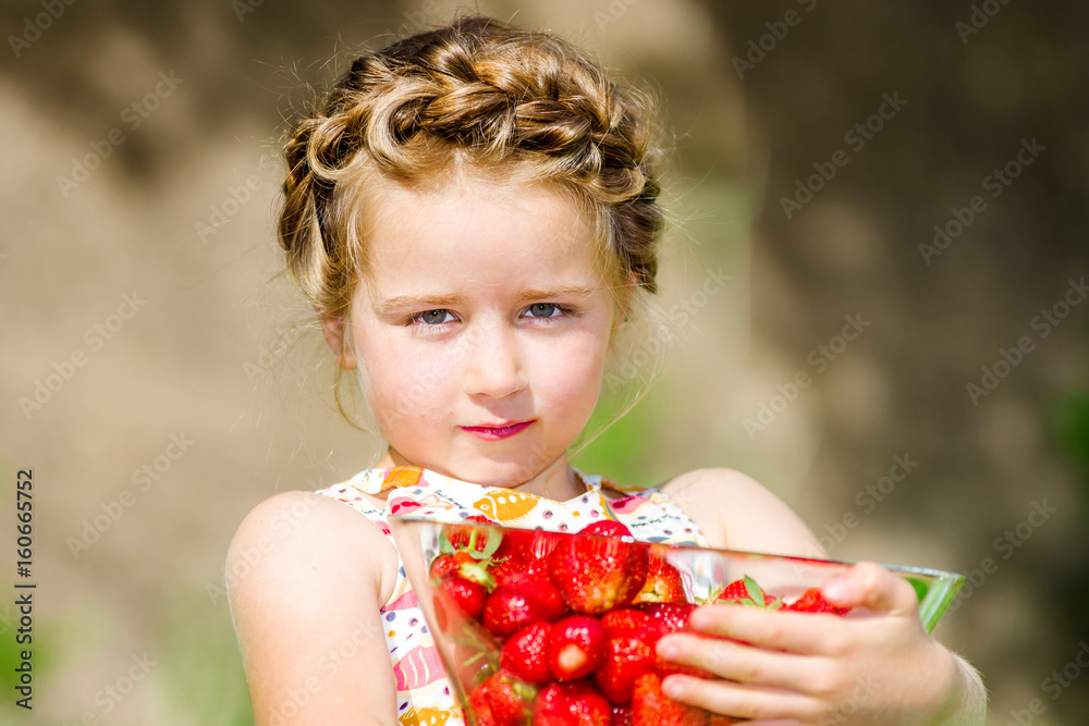 Cute little girl posing with fresh red strawberry in the sunny garden Cute little girl posing with fresh red strawberry in the sunny garden