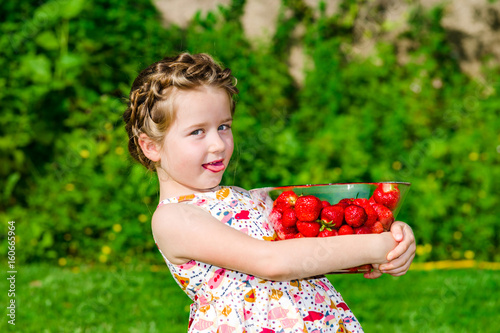 Cute little girl posing with fresh red strawberry in the sunny garden
