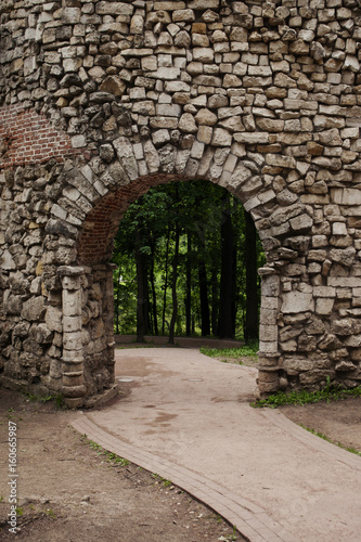 Vertical location of an arch and a stone wall, paths and forests in the background