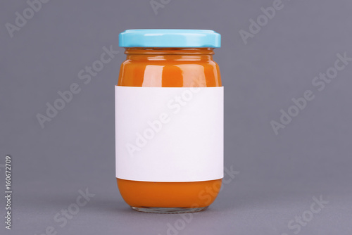 Orange glass jar for baby food bank on grey background. Organic baby food puree. Mock up without template design label.