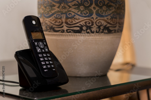 Telephone at hotel room sitting on bedside table with the table lamp.